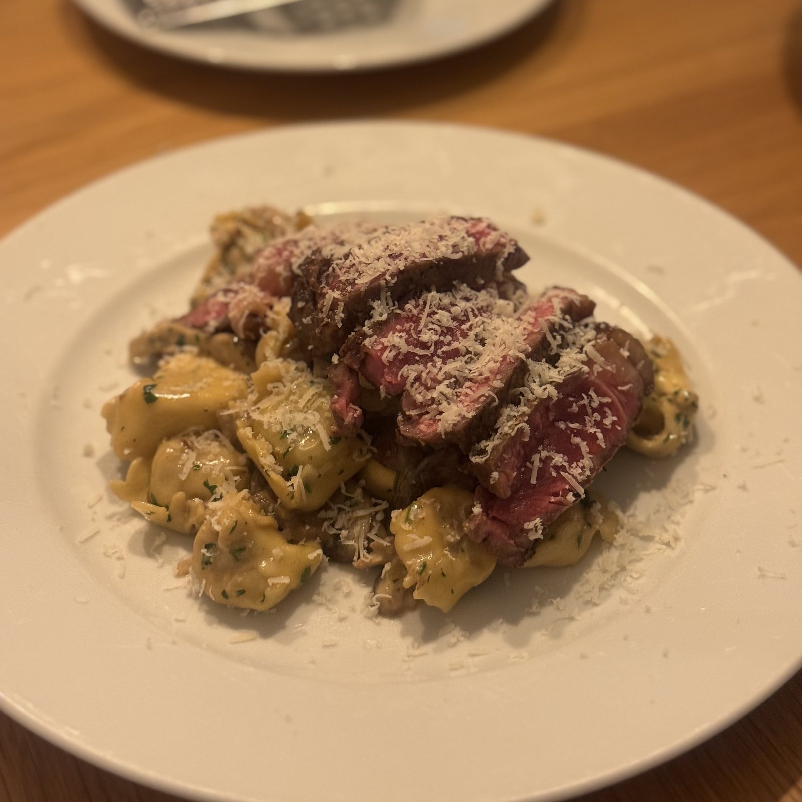 Svamperavioli med champignonsauce, skiver af rosa steak og revet parmesan på en hvid tallerken